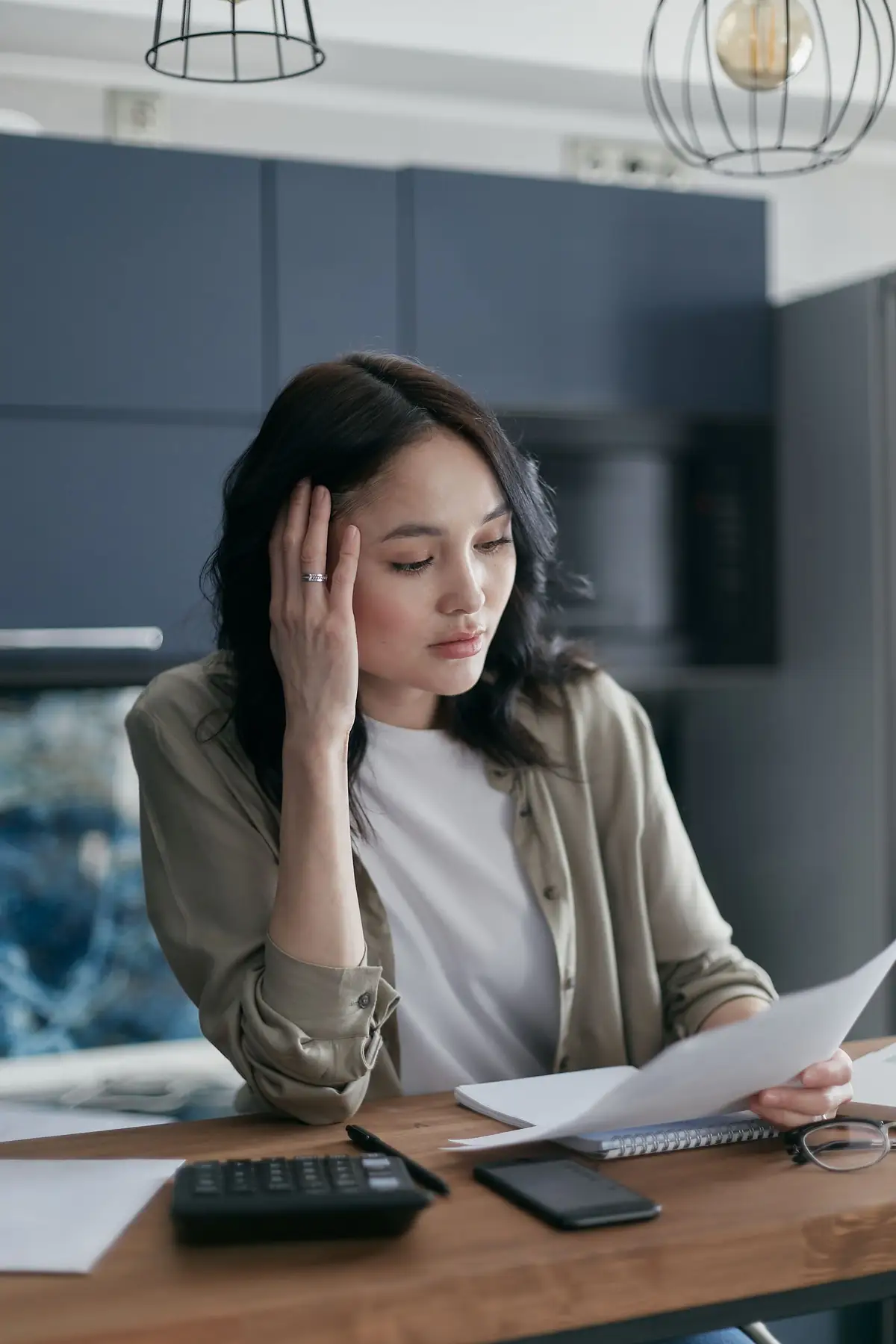 A woman sitting at a kitchen table looking through bills and papers.
